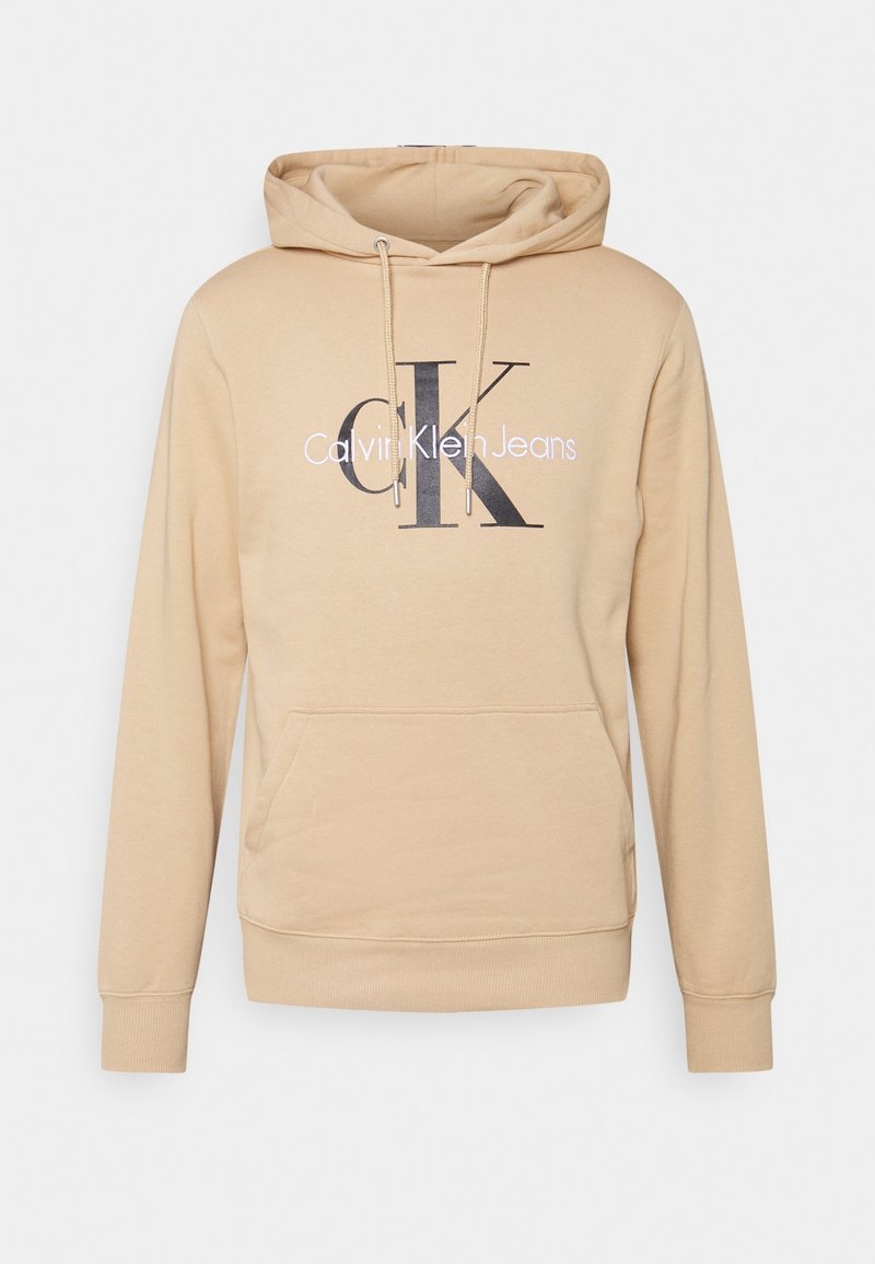 Sweat à capuche beige avec poche avant et cordons, avec de grandes lettres noires "CK" et le texte "Calvin Klein Jeans" sur la poitrine.