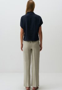 Top corto blu scuro con colletto, abbinato a pantaloni leggeri e larghi di un beige chiaro. Sandali piatti completano l'outfit.