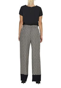 Top noir à manches courtes associé à un pantalon large avec un motif géométrique blanc et des poignets bleu marine aux chevilles.