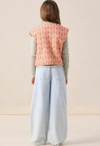 Gilet matelassé orange avec un motif paisley sur une chemise à rayures à manches longues, associé à un jean large bleu clair.