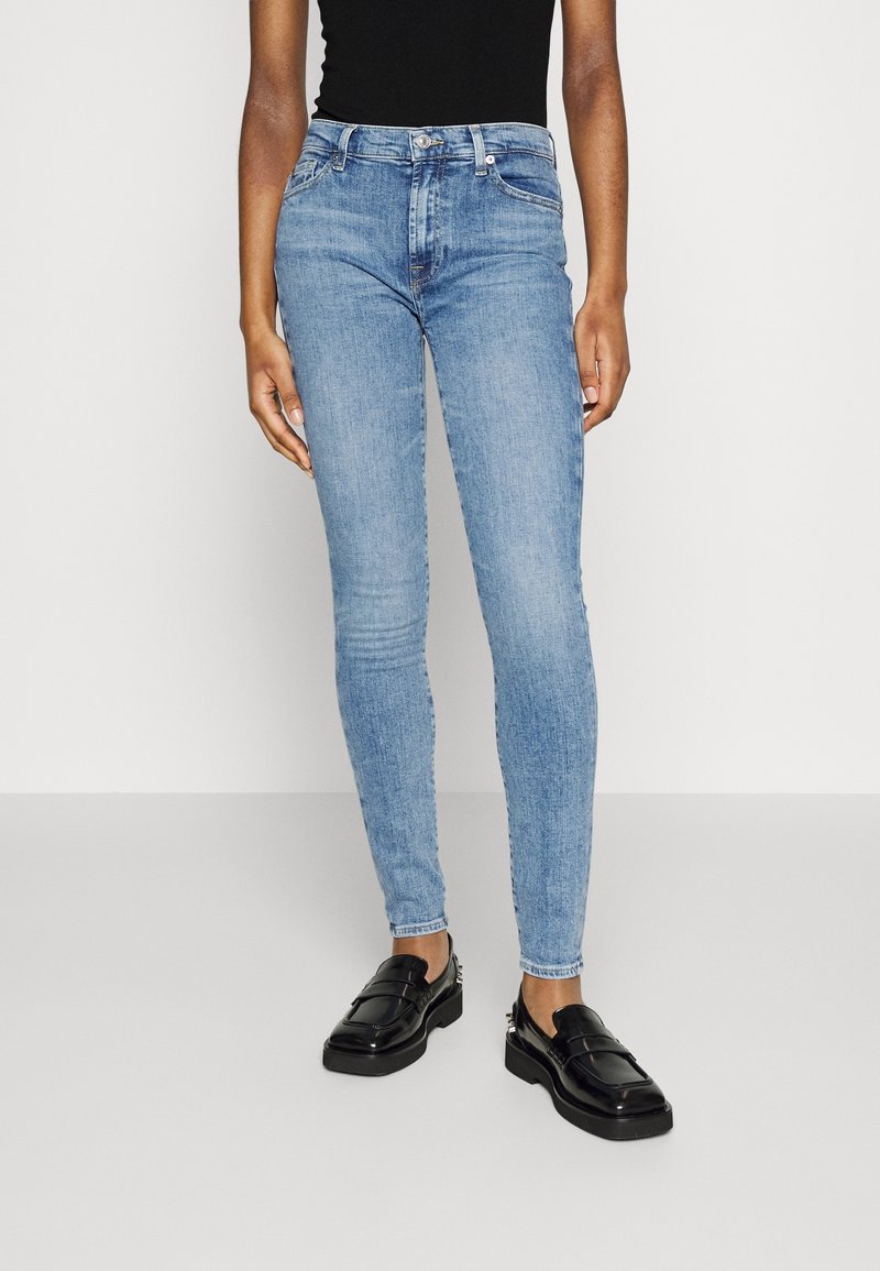 Jeans ajustados en denim azul claro, de cintura alta con bolsillos frontales, combinados con mocasines negros, con una textura suave y zonas deslavadas.