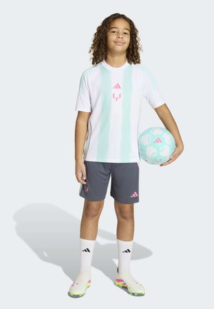 Kind met krullend haar staat en houdt een lichtblauwe en witte voetbal vast, draagt een wit en muntgroen gestreept shirt, grijze korte broek, witte sokken en voetbalschoenen.