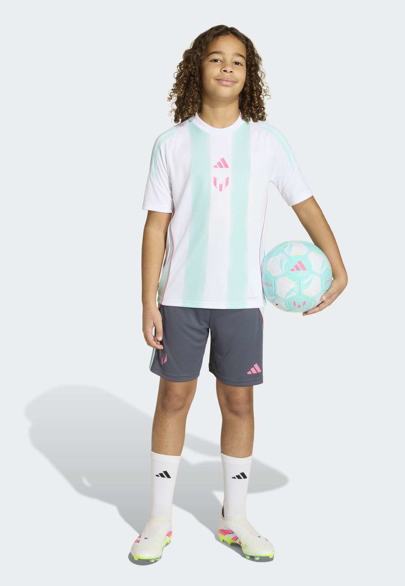 Enfant aux cheveux bouclés tenant un ballon de football bleu clair et blanc, portant un maillot rayé blanc et menthe, un short gris, des chaussettes blanches et des crampons.