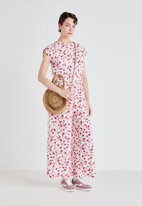 Jumpsuit floreale bianco con motivi rosa, maniche a cappuccio e vestibilità comoda. Abbinato a una borsa rotonda intrecciata e sneakers viola chiaro.