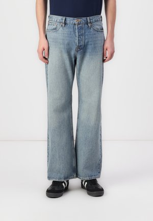 Baggy lyseblå denimjeans med rett benpassform, fem lommer, synlig søm og knapp- og glidelås-stengning. Brukes med svarte sneakers.