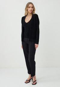 Cardigan nero aperto davanti in maglina texturizzata, indossato sopra un top a scollo a v coordinato. Abbinato a pantaloni neri skinny e sandali con cinturini.