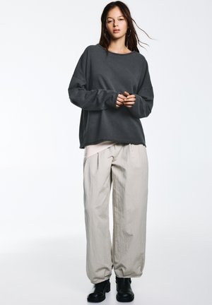 Sötétszürke, túlméretezett pulóver hosszú ujjakkal, világos bézs, laza szabású nadrággal párosítva. Fekete bokacsizma egészíti ki a szettet.