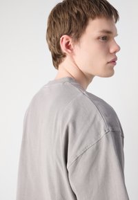 Lys grå oversized bomulds t-shirt med korte ærmer og rund hals. Har en blød tekstur og synlige sømme langs skuldrene.