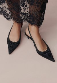 Mustat slingback-kengät, joissa on terävä kärki, koristeltu helmiäisillä ja kukkakuviolla, matalalla korolla ja mattapinnalla.