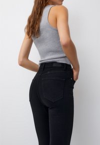Jeans negros de cintura alta con un diseño ceñido, estilo clásico de cinco bolsillos y una textura suave. Llevado con una camiseta sin mangas de canalé gris.