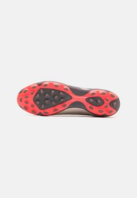 Semelle de chaussure avec une base noire et des accents rouges, dotée de crampons ronds pour une meilleure adhérence et d'un design lisse et contour pour optimiser la performance.