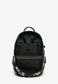 Sac à dos avec un motif floral à l'extérieur. L'intérieur est doté d'une doublure noire, d'un compartiment rembourré et d'une poche en maille. Fermeture à glissière.
