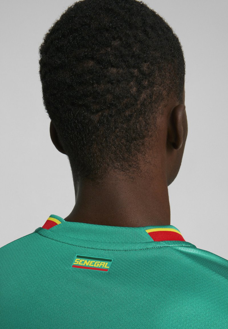 Turkis sportstrøje med en rød og gul stribet krave, der har et "SENEGAL" mærke på bagsiden. Glat stoftekstur.