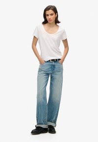 Camiseta blanca de escote redondo, jeans de pierna ancha azul claro con un lavado desgastado, zapatos de cuero negros, complementados con un cinturón negro.