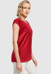 Rød kortærmet V-hals T-shirt, lavet af blødt materiale, med en afslappet pasform og en glat tekstur, parret med hvide bukser.