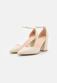 Beige korkokengät, joissa on terävä nenä, nilkkaremmillä ja teksturoidulla pinnalla. Varustettu tukevalla koron ja sileällä sisävuorella.
