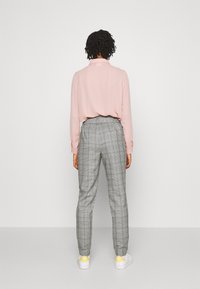 Ljust rosa långärmad skjorta instoppad i grå rutiga byxor. Byxorna har en avsmalnande ben och platt midja, i kombination med vita sneakers.