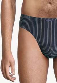 Marine gestreepte zwemslip met een low-rise ontwerp, elastische tailleband en fijne verticale strepen in lichtblauw en groen.