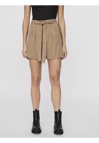 Shorts taille haute beiges avec des plis et une ceinture nouée. Fabriqués en tissu doux, présentant un design simple et une coupe décontractée. Bottines noires montrées.