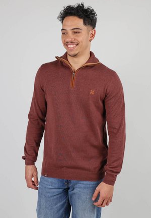Pull en maroon avec un col montant, présentant une demi-fermeture éclair et un accent marron au col. Fabriqué dans un tissu tricoté texturé.