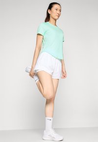 Mint zelena majica s kratkimi rokavi v kombinaciji z belimi kratkimi hlačami. Majica ima okrogel rob; model nosi bele atletske nogavice in teniske.