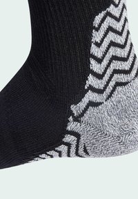 Calcetín negro con un diseño de punto texturizado y un patrón en zigzag blanco alrededor del tobillo. El material parece elástico y transpirable.