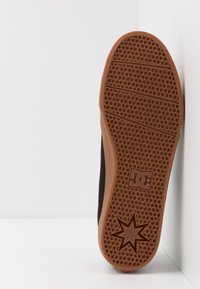 Black skate shoe with a textured brown rubber sole featuring a star pattern and logo. The design emphasizes grip and durability.