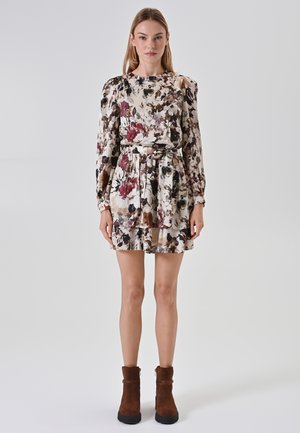 Bloemendruk jurk met lange mouwen, een ceintuur in de taille en een gelaagde rok. Kleuren zijn crème, bordeauxrood en donkergroen. Draagt met bruine enkellaarsjes.