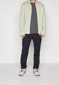 Chaqueta de cremallera color beige claro, camiseta gris, pantalones negros y zapatillas gris con detalles beige. Tejido suave, corte relajado, sin logotipos visibles.