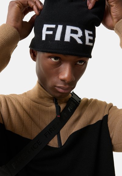 Sort strikket hue med hvid "FIRE" tekst; tan ribbet sweater med sorte accenter og lynlås i halsen; justerbar rem med præget logo.