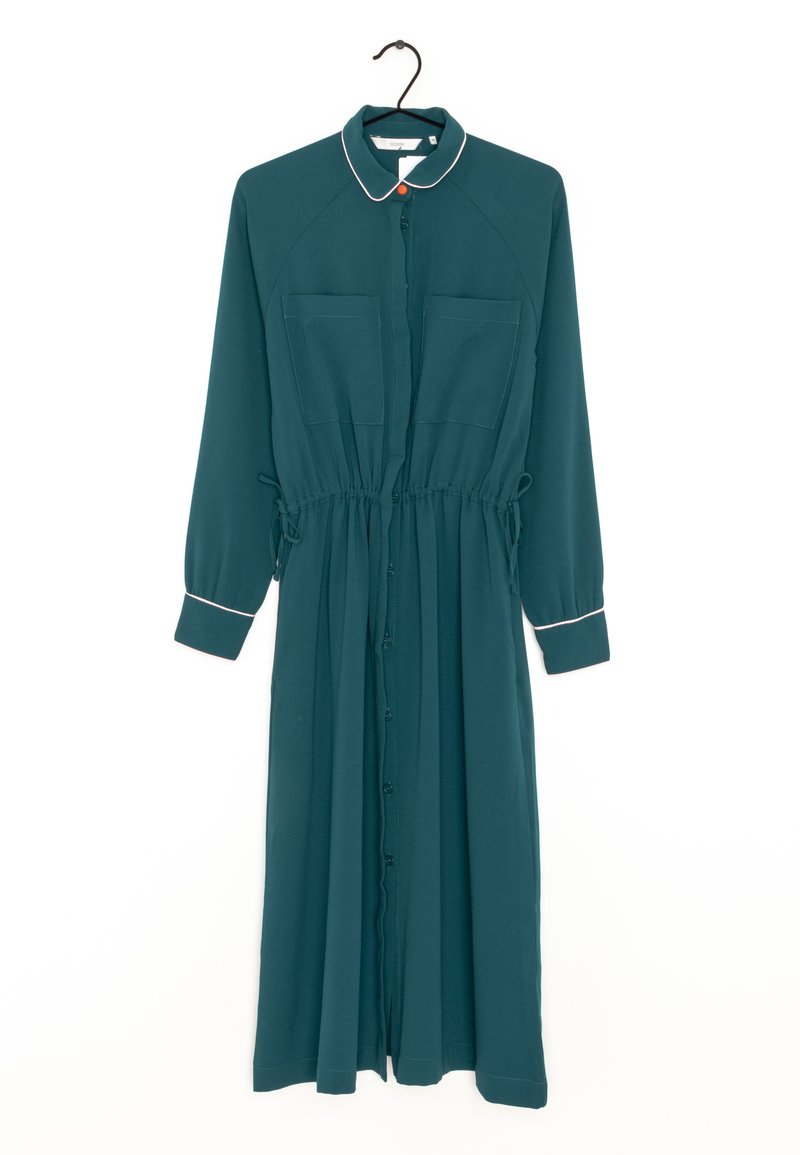 Robe midi à manches longues couleur sarcelle avec boutons sur le devant, deux poches poitrine, liens à la taille, bordure blanche sur le col et les poignets, suspendue à un cintre noir.