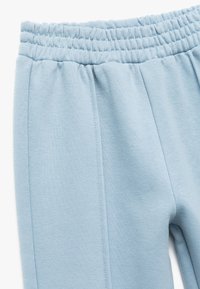 Jasnoniebieskie spodnie dresowe z elastyczną talią, wykonane z miękkiego, teksturowanego materiału, z bocznymi szwami. Prosty, elegancki fason.