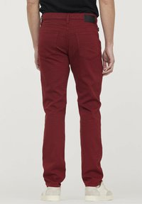 Pantalons en coton rouge avec une coupe slim, dotés de deux poches arrière et d'une étiquette noire au niveau de la taille. Texture lisse et design de jambe fuselée.