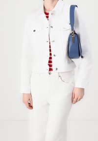 Biała dżinsowa kurtka z srebrnymi guzikami, zestawiona z białymi spodniami i czerwoną bluzką w paski. Na ramieniu noszona jest niebieska torebka typu crossbody.