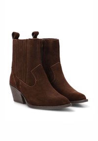 Botas de tobillo de ante marrón con punta afilada, que cuentan con paneles laterales, cierre de cremallera y tacón apilado. El material texturizado añade profundidad.