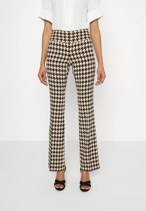 Vrouw draagt hooggetailleerde, beige en zwarte rechte broek met pied-de-poule-patroon, zwarte open-toe hakken en een wit kort mouwig blouseje.