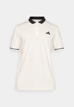 Camisa polo creme com colarinho preto e riscas. Veste-se com uma pala de três botões. O lado esquerdo do peito apresenta um logo da Adidas em preto. Textura de tecido macio.