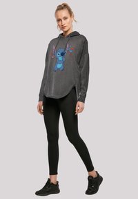 Šedá mikina s oversized střihem, zdobená modrým karikaturním motivem. V kombinaci s černými legínami a černými sportovními botami.