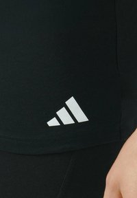 Maglietta sportiva nera con una texture liscia, caratterizzata da un logo bianco a tre strisce ben visibile sul lato sinistro in basso.