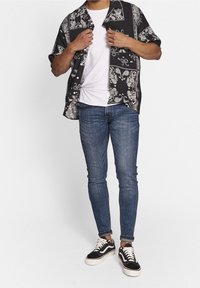 Camisa de manga corta con estampado en blanco y negro sobre una camiseta blanca, combinada con vaqueros de mezclilla azul y zapatillas negras con suelas blancas.