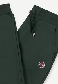 Ciemnozielone spodnie dresowe z prążkowanym paskiem i ściągaczami, sznurkiem do wiązania, bocznymi kieszeniami oraz okrągłą naszywką z logo "COLMAR" w pobliżu kieszeni.