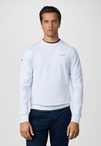 Sudadera de color azul claro con mangas largas, cuello redondo y puños acanalados. Presenta un pequeño logo "Hackett" en el pecho y un acento verde.