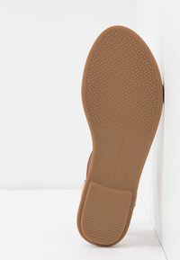Semelle de chaussure marron avec motif de grip texturé et marquage "Tommy Hilfiger", photographiée verticalement sur fond blanc.