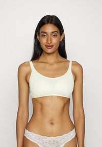 Sostén inalámbrico color amarillo claro con tirantes anchos y textura suave, que presenta un diseño sin costuras y un estilo minimalista.