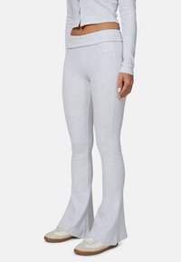 Szare dzwonowate spodnie dresowe wykonane z miękkiego materiału, z szerokim pasem na wysokości talii i pionowymi szwami. W połączeniu z jasnymi sneakersami, tworzą swobodny styl.