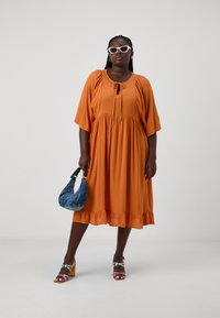 Vestido laranja até ao joelho com corpete franzido, mangas curtas e bainha plissada. Combinado com uma mala azul e sandálias de salto multicoloridas.