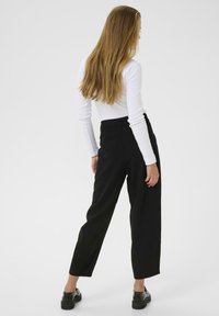 Pantalons noirs taille haute à coupe décontractée, avec un tissu lisse, une silhouette fuselée et un dos épuré. Associés à un haut blanc.