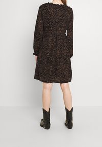 Svart klänning med brun leopardtryck, långa ärmar och midjeband. Har en utsvängd kjol och en scalloperad halsringning. Bärs med svarta stövlar.