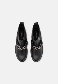 Bottes noires à la cheville avec une finition en cuir lisse, ornées d'une chaîne en argent décorative à l'avant et de panneaux latéraux élastiques pour un enfilage facile.