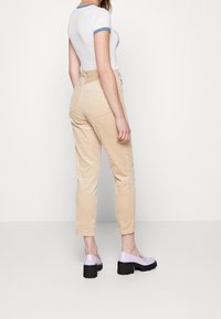 Pantalons en velours côtelé beige avec une coupe droite, poches arrière, associés à des chaussures à plateforme brillantes lavande et une chemise blanche à bordures bleues.